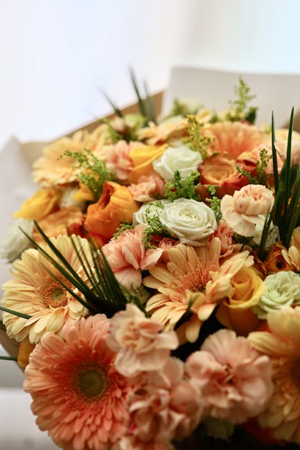 A vibrant floral bouquet featuring a mix of soft peach, cream, and pale pink roses, complemented by light peach gerbera daisies and green foliage, arranged in a lush, harmonious display. The flowers a
