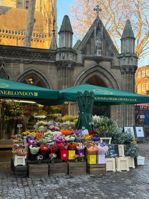 An outdoor flower stall in front of a historic stone church with Gothic architectural details, including pointed arches and spires, during daytime. The stall features a variety of fresh floral arrange